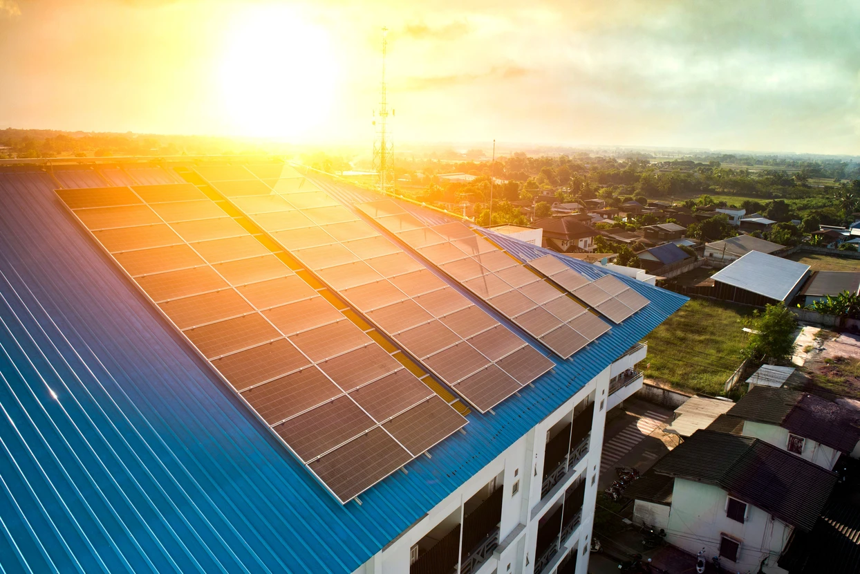 Vue aérienne d'un bâtiment commercial équipé de panneaux solaires photovoltaïques sur toiture bleue ondulée, au coucher du soleil
