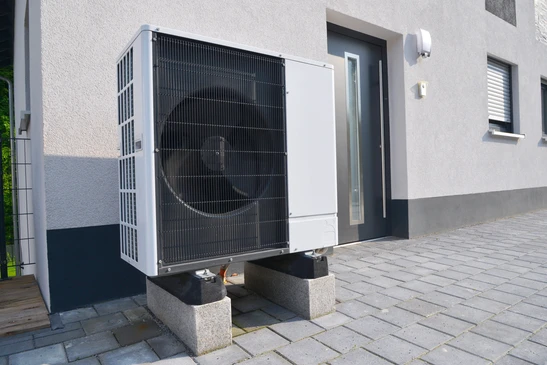 Ext&eacute;rieur r&eacute;sidentiel moderne avec pompe &agrave; chaleur air-eau install&eacute;e sur socle b&eacute;ton devant maison contemporaine