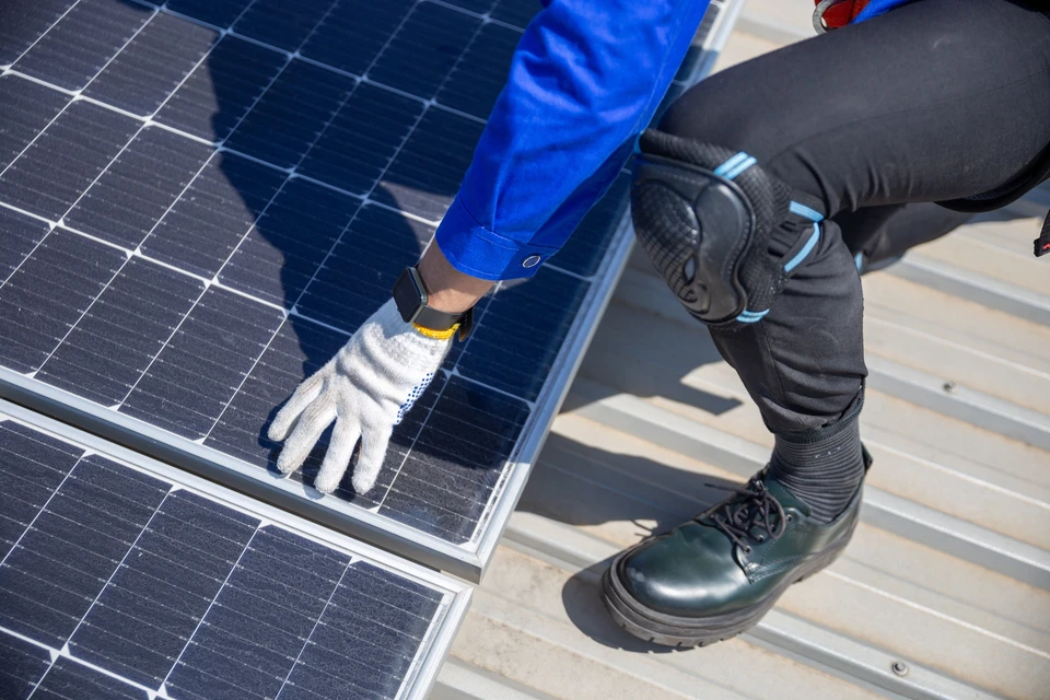 Technicien en combinaison bleue installant des panneaux solaires photovoltaïques sur toiture