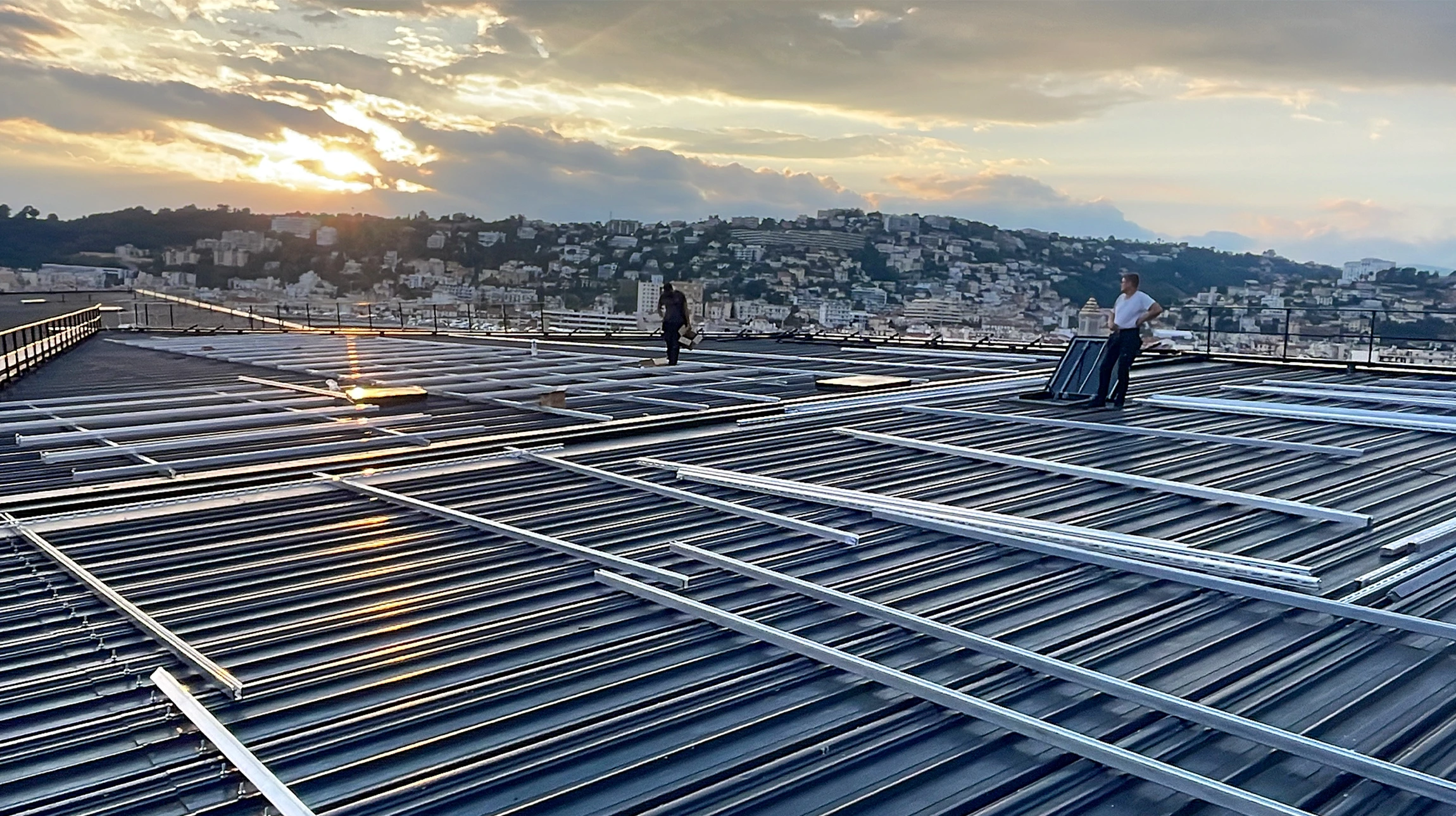 Vue a&eacute;rienne d'un b&acirc;timent commercial &eacute;quip&eacute; de panneaux solaires photovolta&iuml;ques sur toiture bleue ondul&eacute;e, au coucher du soleil
