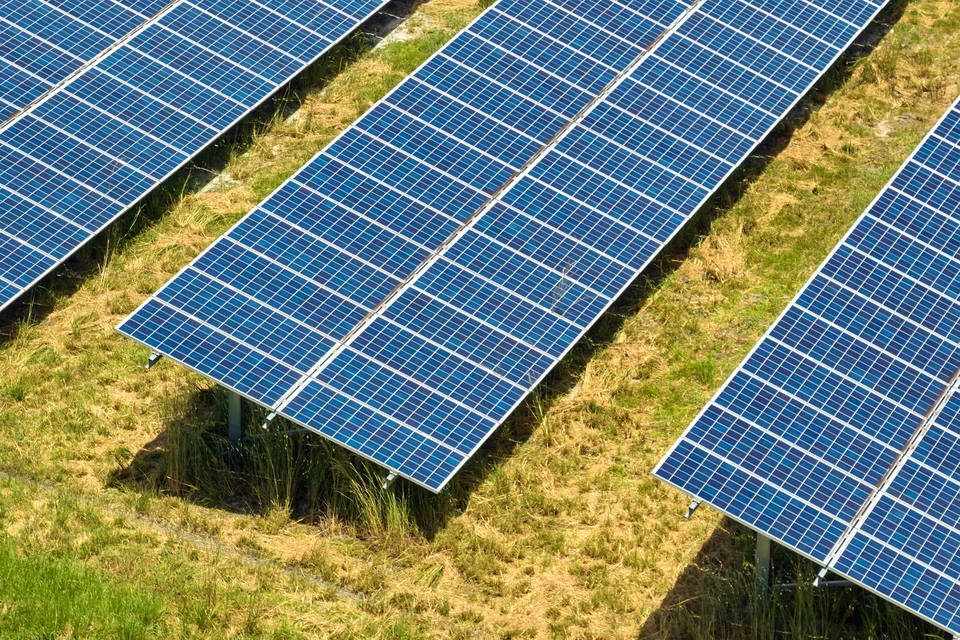 Technicien en combinaison de travail grise et jaune effectuant la maintenance d'une installation solaire photovoltaïque sur toiture, sous ciel bleu nuageux