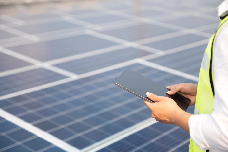 Deux techniciens en équipements de protection individuelle inspectent une installation solaire photovoltaïque sous un ciel nuageux