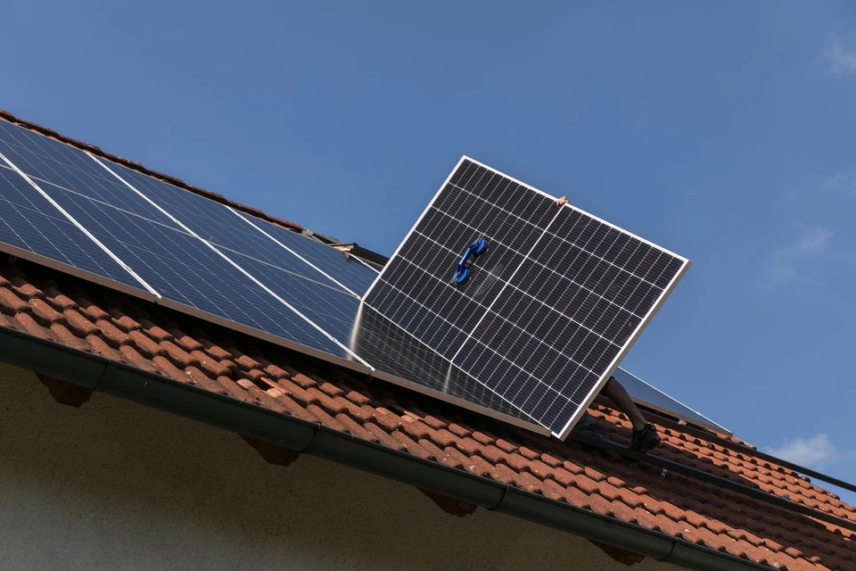 Deux techniciens installent un panneau solaire photovoltaïque sur une toiture résidentielle au coucher du soleil